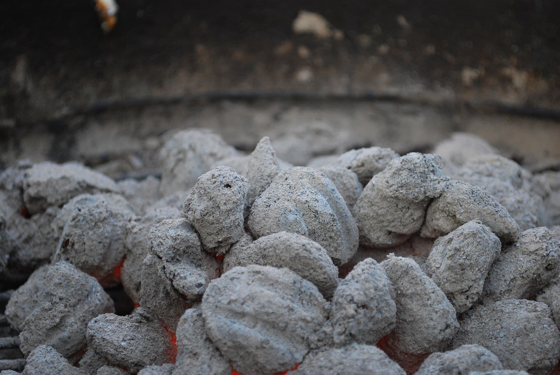 Close-up of ash-grey charcoal briquettes with an orange glow showing through the ash